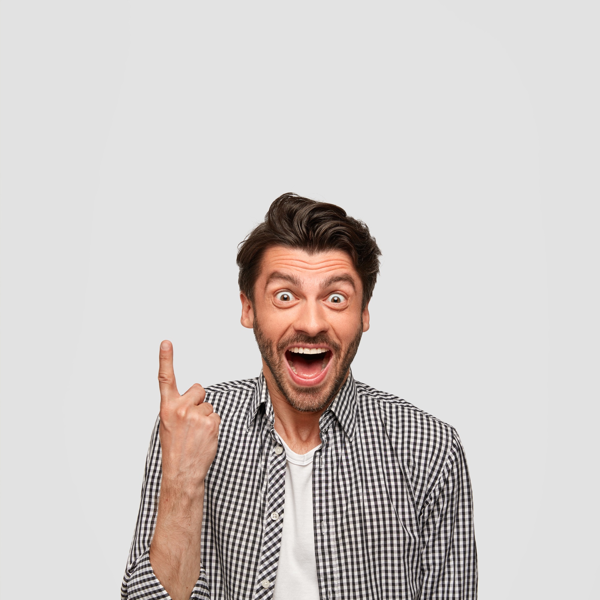 Image of joyful happy young Caucasian male with surprised expression, points upwards, stares with bu