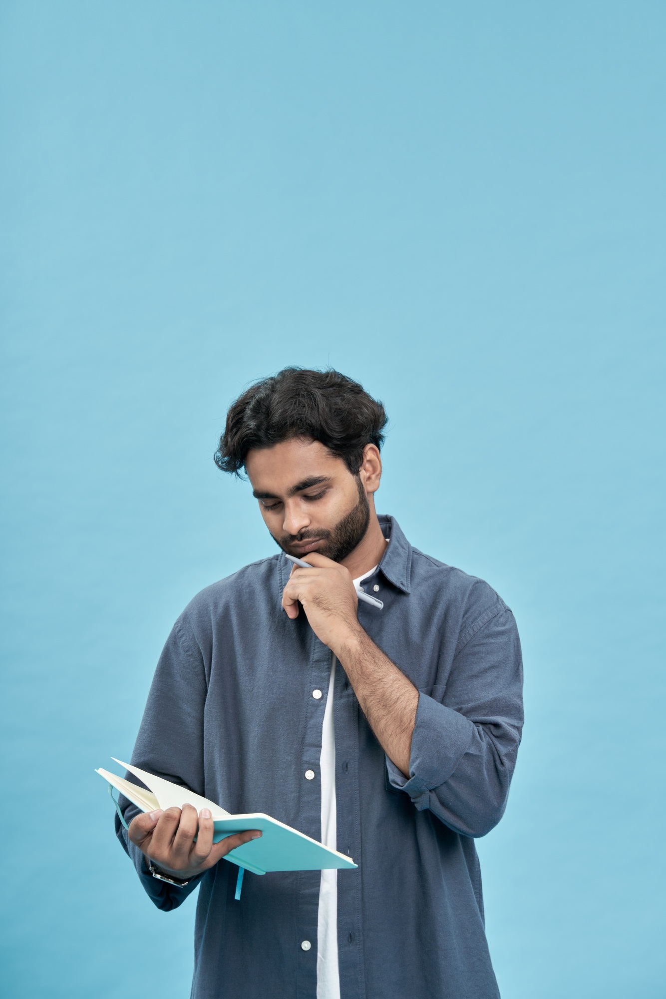 Thoughtful young arab man student writing in notebook isolated on blue.