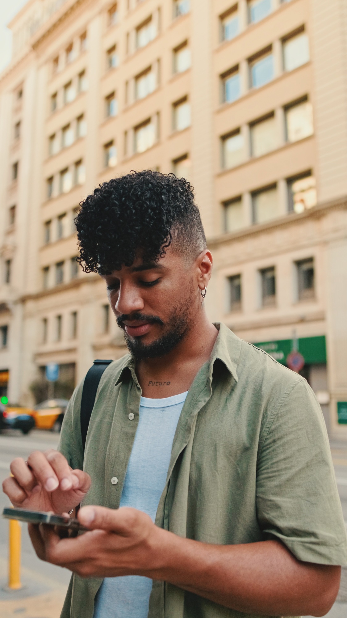 Young smiling man with beard dressed in an olive color shirt uses phone